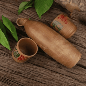 Wooden bottle and two decorated wooden cups on rustic wooden table with green leaves