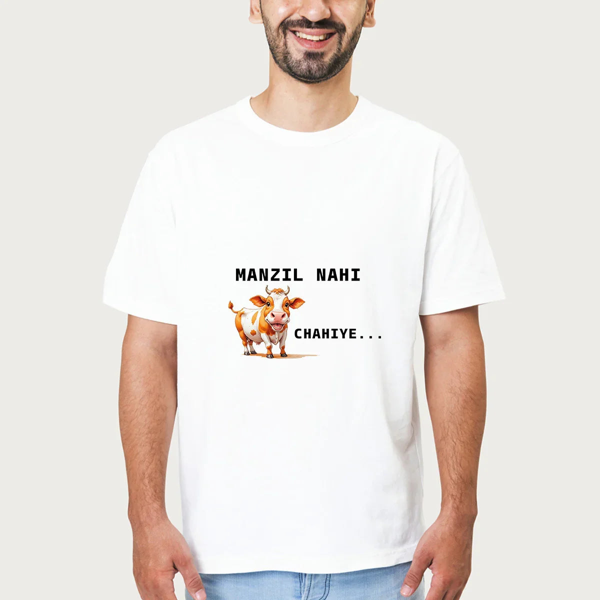 Smiling man wearing white T-shirt with cartoon cow and text Manzil Nahi Chahiye