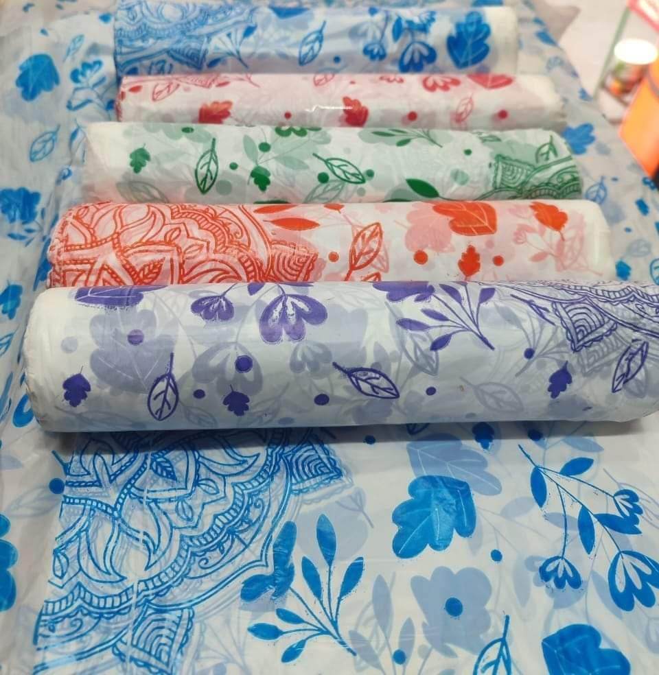 Colorful floral and leaf printed fabric rolls arranged on matching patterned cloth